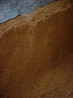 「肥料」である。あったかご飯にふりかけたい美味しいそうな香りを放つ松下くん独自の肥料である。 原料は米糠と魚粕に研究に研究を重ねて作った複合菌類によって発酵させたものである。今年は４月の気温が例年より高いため発酵スピードが早く、おかげで仕事がよく進むらしい。一反あたり約１２０〜１３０キロくらい田植え前のこの時期に撒くのである。寒冷な地方なら秋に行う作業であるが気温の高い静岡ならこの時期で充分に間に合う。田圃に撒かれた肥料は土中の細菌類とあいまってさらに発酵分解を始め栄養たっぷりのスープをこしらえて田植えの